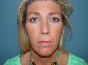 A woman wearing a green shirt and a green necklace is looking at the camera.