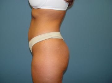 A woman in a white bra and white thong is standing in front of a blue wall.