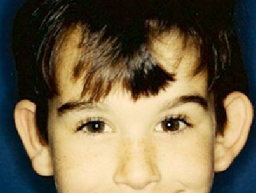 A close up of a young boy 's face with a blue background.