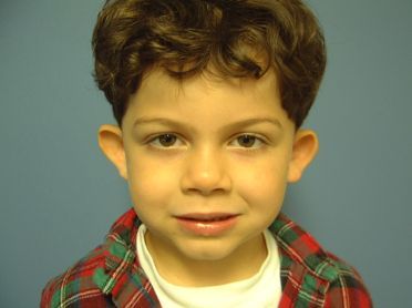 A young boy wearing a plaid shirt and a white shirt is looking at the camera.