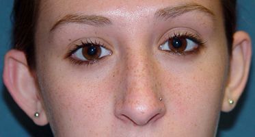 A close up of a woman 's face with a nose ring and earrings.