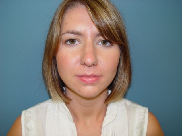 A woman in a white shirt is standing in front of a blue wall.