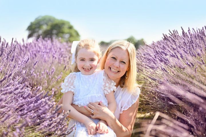 Mother and child smiling in a lavender field, both wearing white, sunny day.