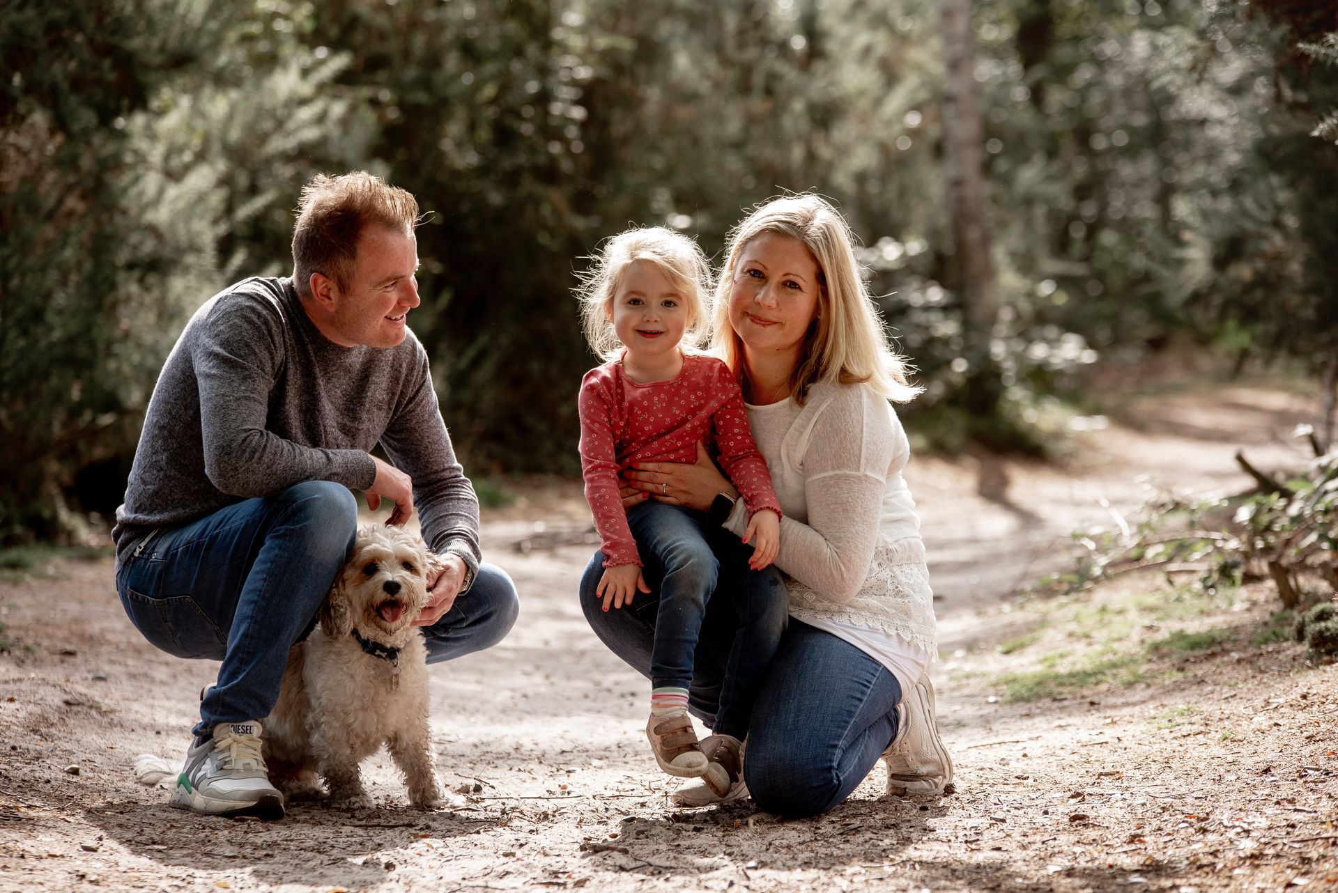 Sarah Gearings family, including a dog, poses on a forest path. Smiling, they are in casual clothes.