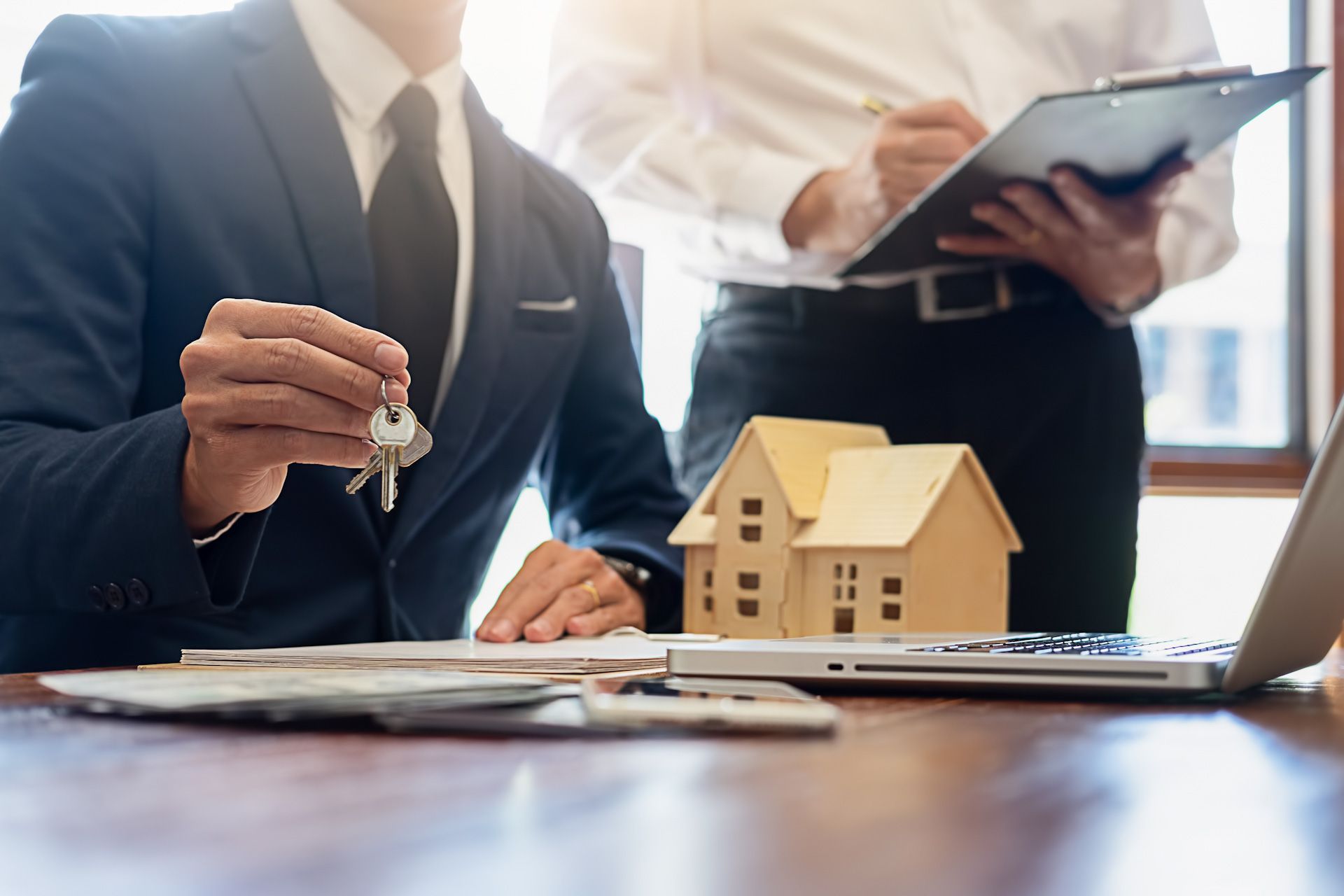 Two men are sitting at a table with a laptop and a model house.