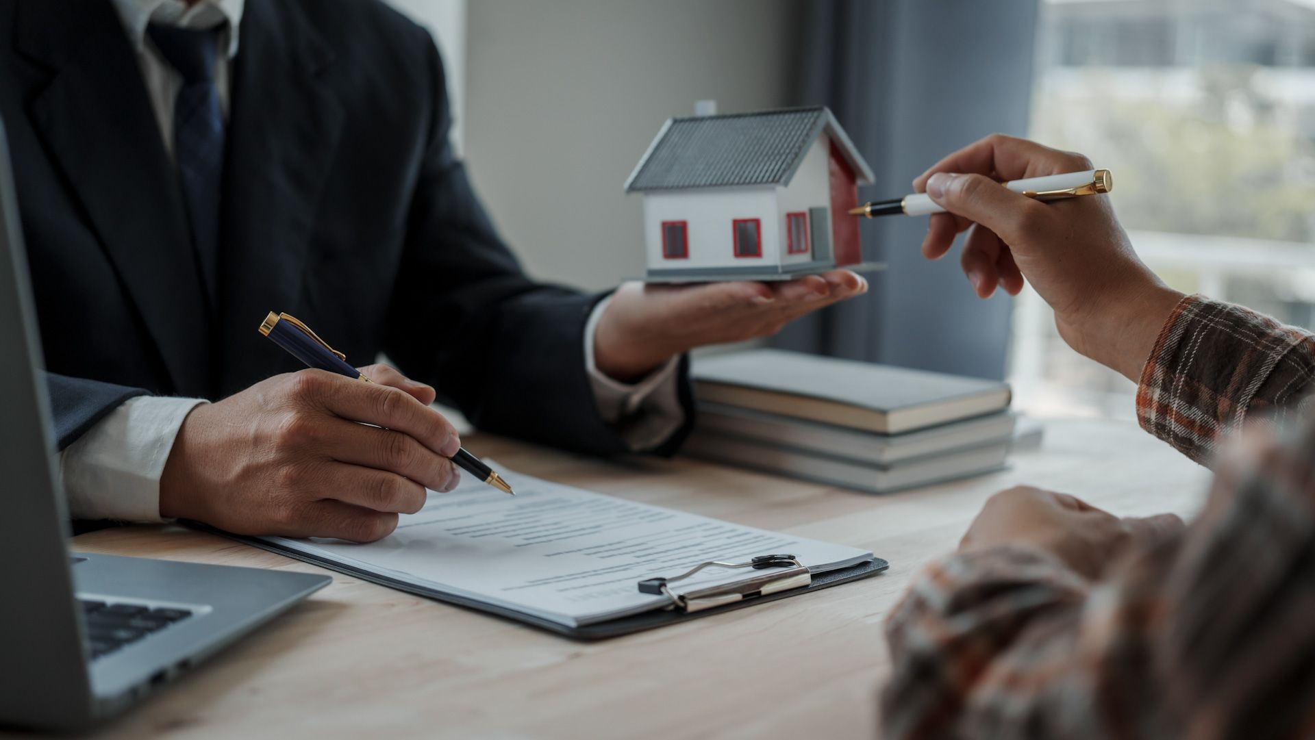 A man is holding a model house in his hand while a woman signs a document.