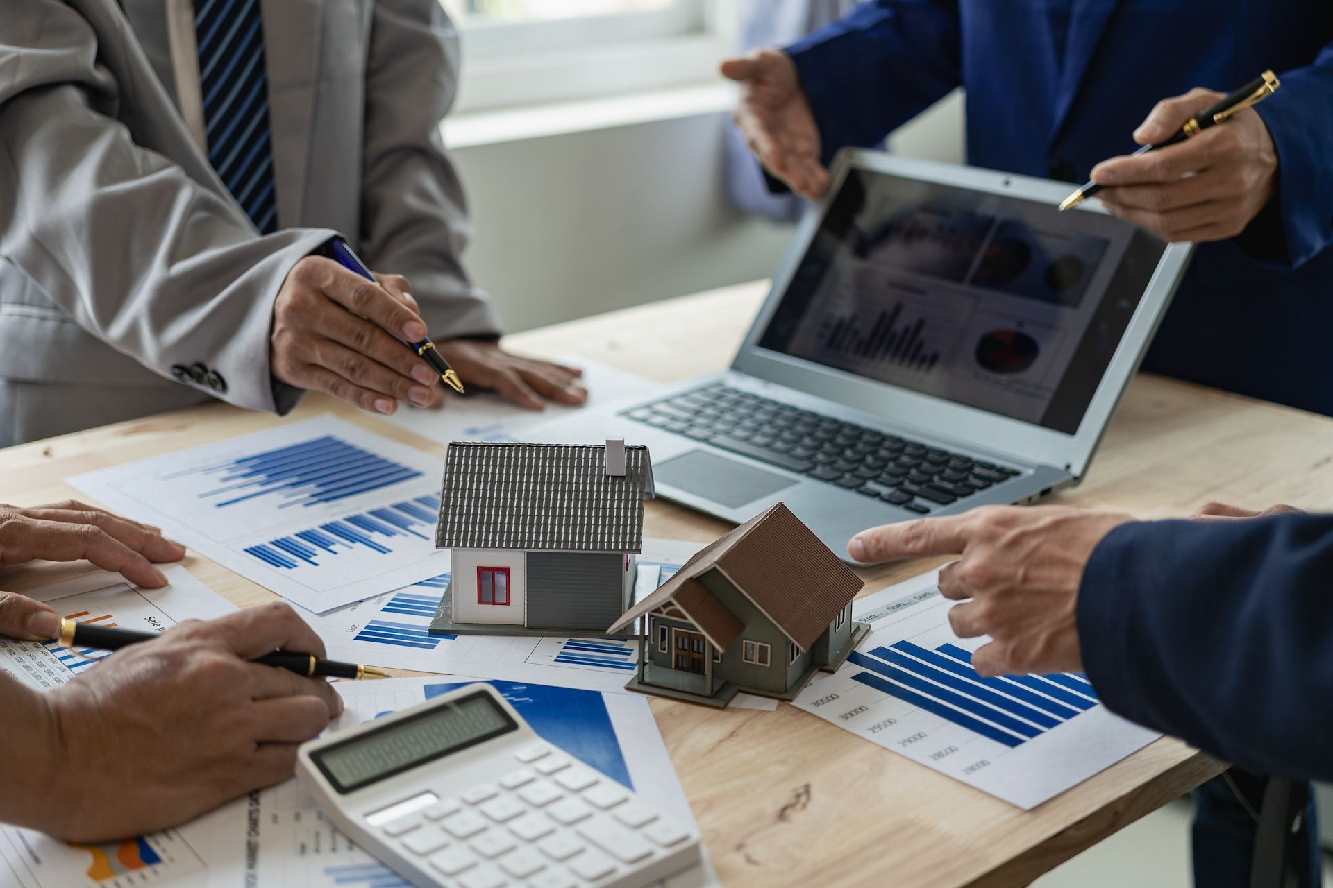 A group of people are sitting at a table with a laptop , calculator , and model houses.