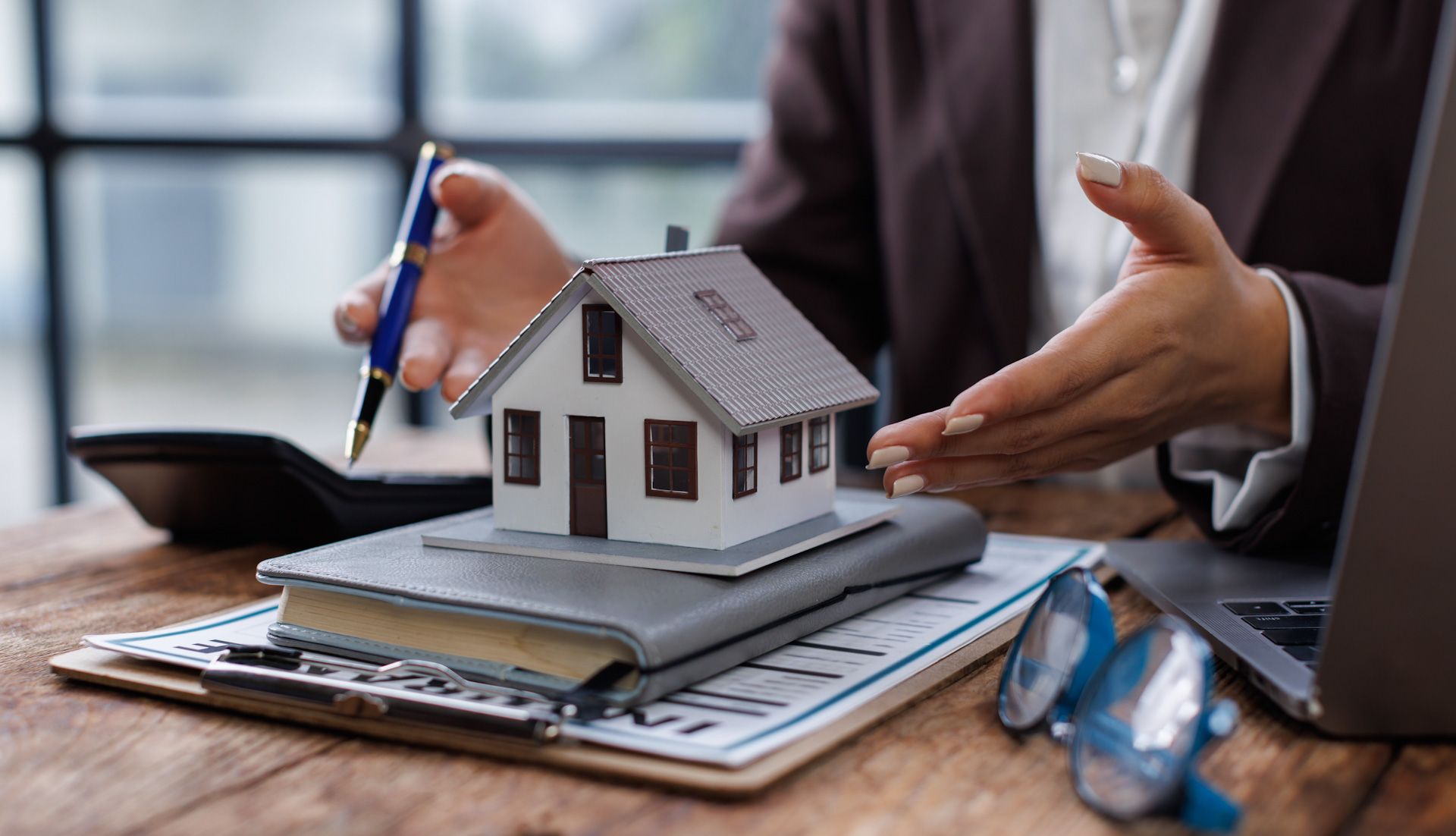 A woman is sitting at a table holding a pen and a model house.