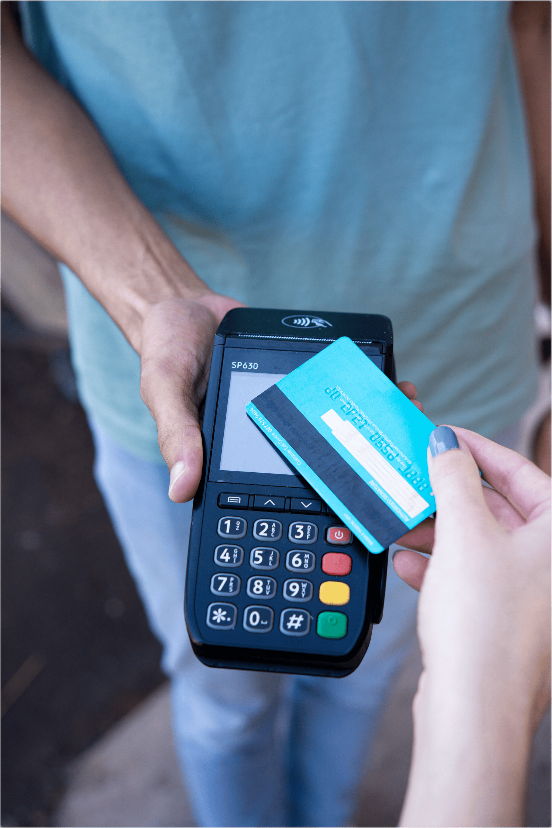 A person holding a card payment terminal while another person taps a blue bank card against the screen to pay.