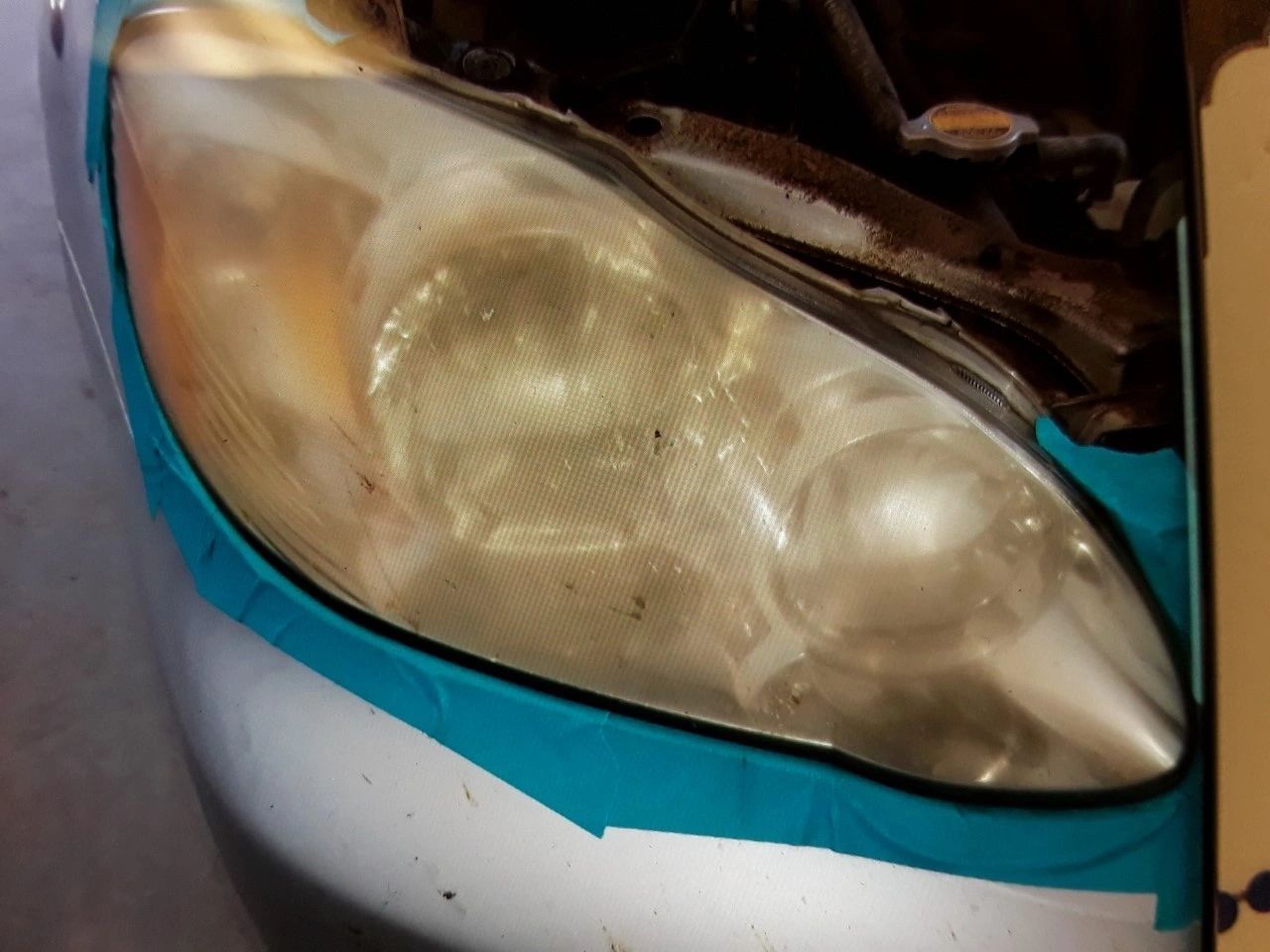 Cloudy, yellowed car headlight taped for restoration on a silver car | Highlift Auto Service