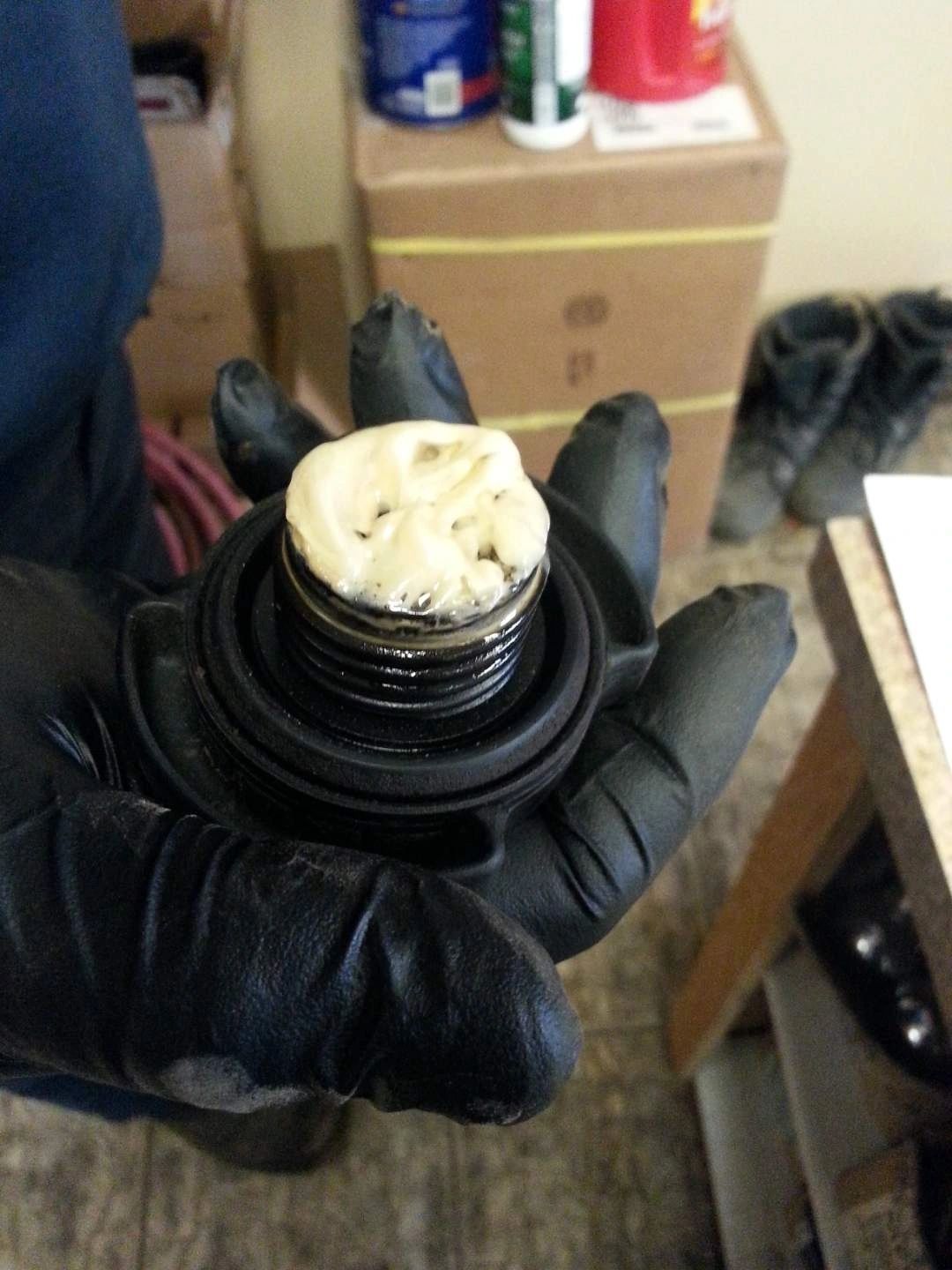 Gloved hand holding a black oil cap with white, foamy sludge on top | Highlift Auto Service