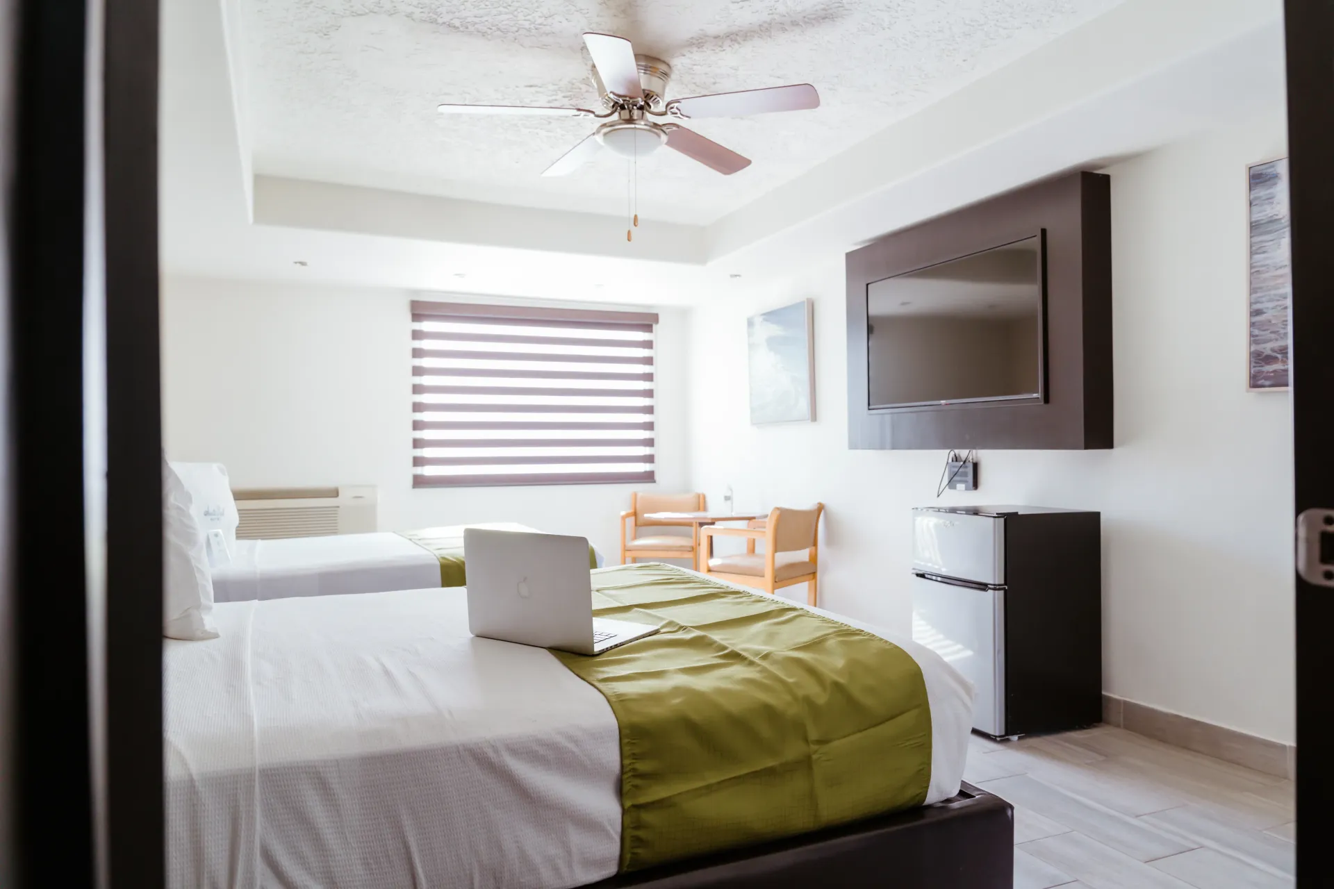 A hotel room with two beds , a ceiling fan and a flat screen tv.