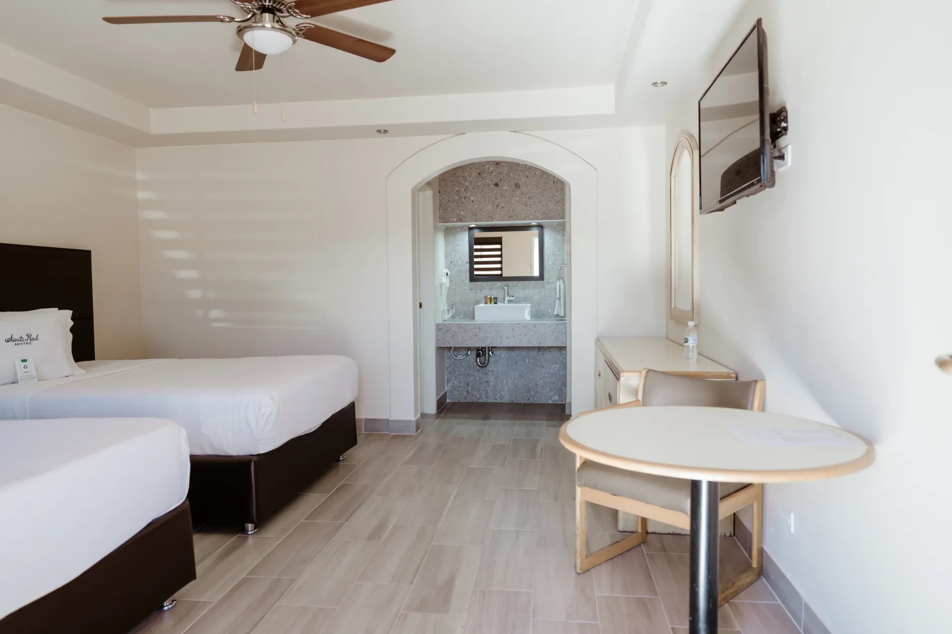 A hotel room with two beds , a table and a television.