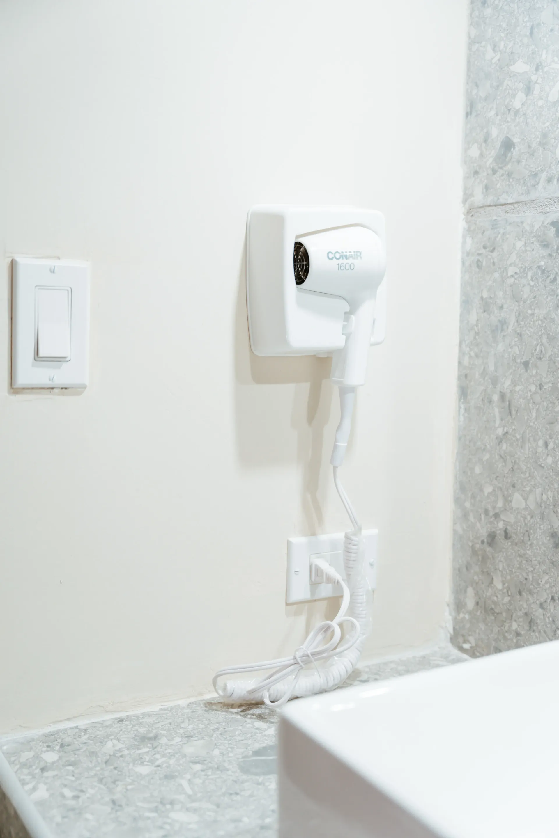 Un secador de pelo está colgado en la pared de un baño, al lado de un lavabo.