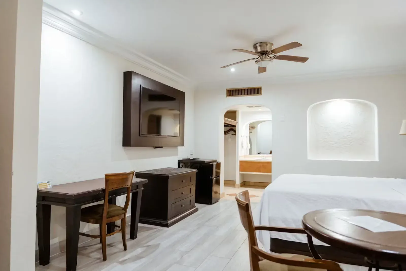 A hotel room with a bed , desk , chairs , television and ceiling fan.