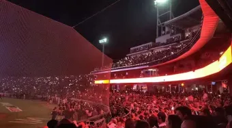 Una multitud de personas está viendo un partido de béisbol en un estadio por la noche.