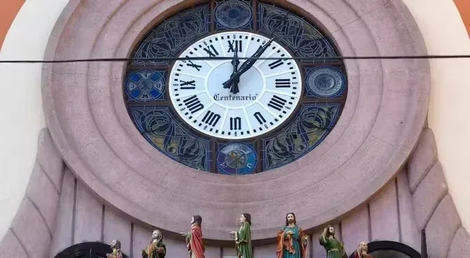 Un reloj con números romanos y un belén delante.
