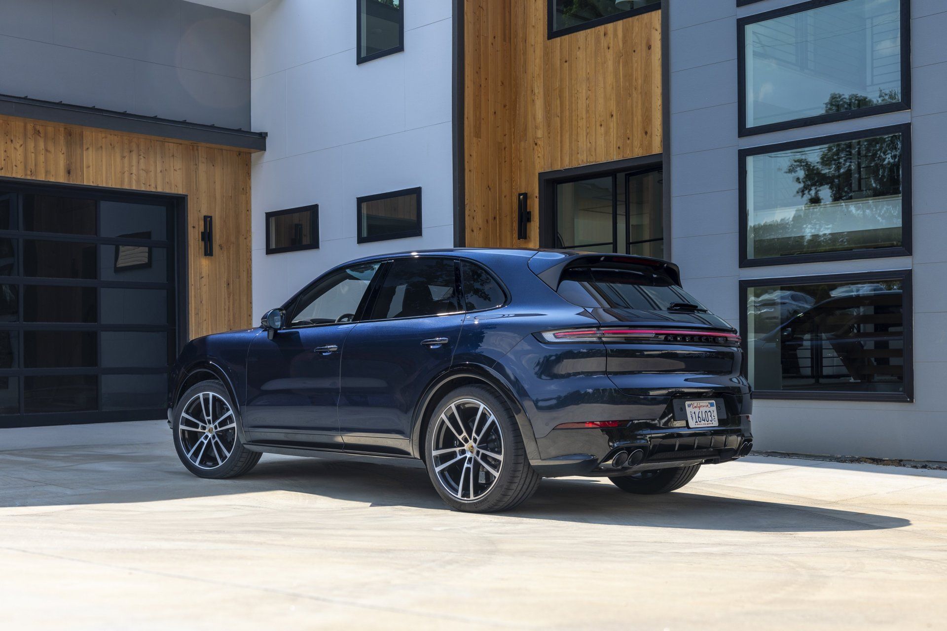Dunkelblauer Porsche-SUV, geparkt vor einem modernen Haus mit Holz und großen Fenstern.
