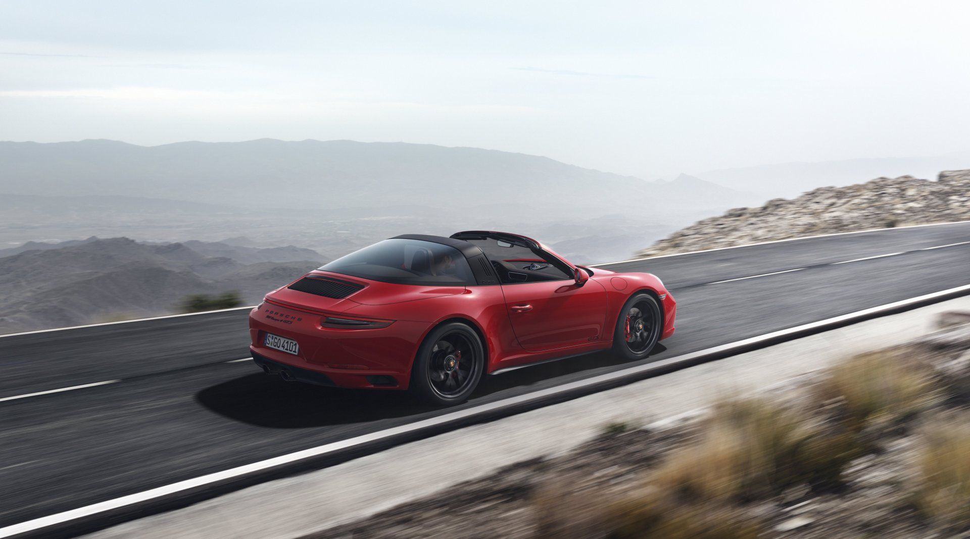 Roter Porsche Targa fährt auf einer Bergstraße mit Landschaftshintergrund.