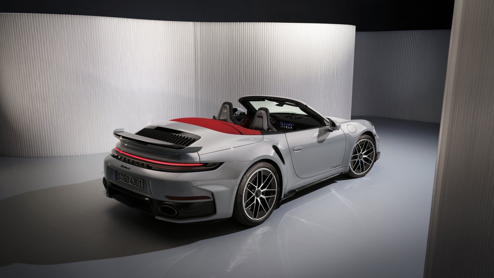 Silbernes Porsche 911 Cabrio mit rotem Verdeck, geparkt in einem Studio mit strukturierten weißen Wänden.