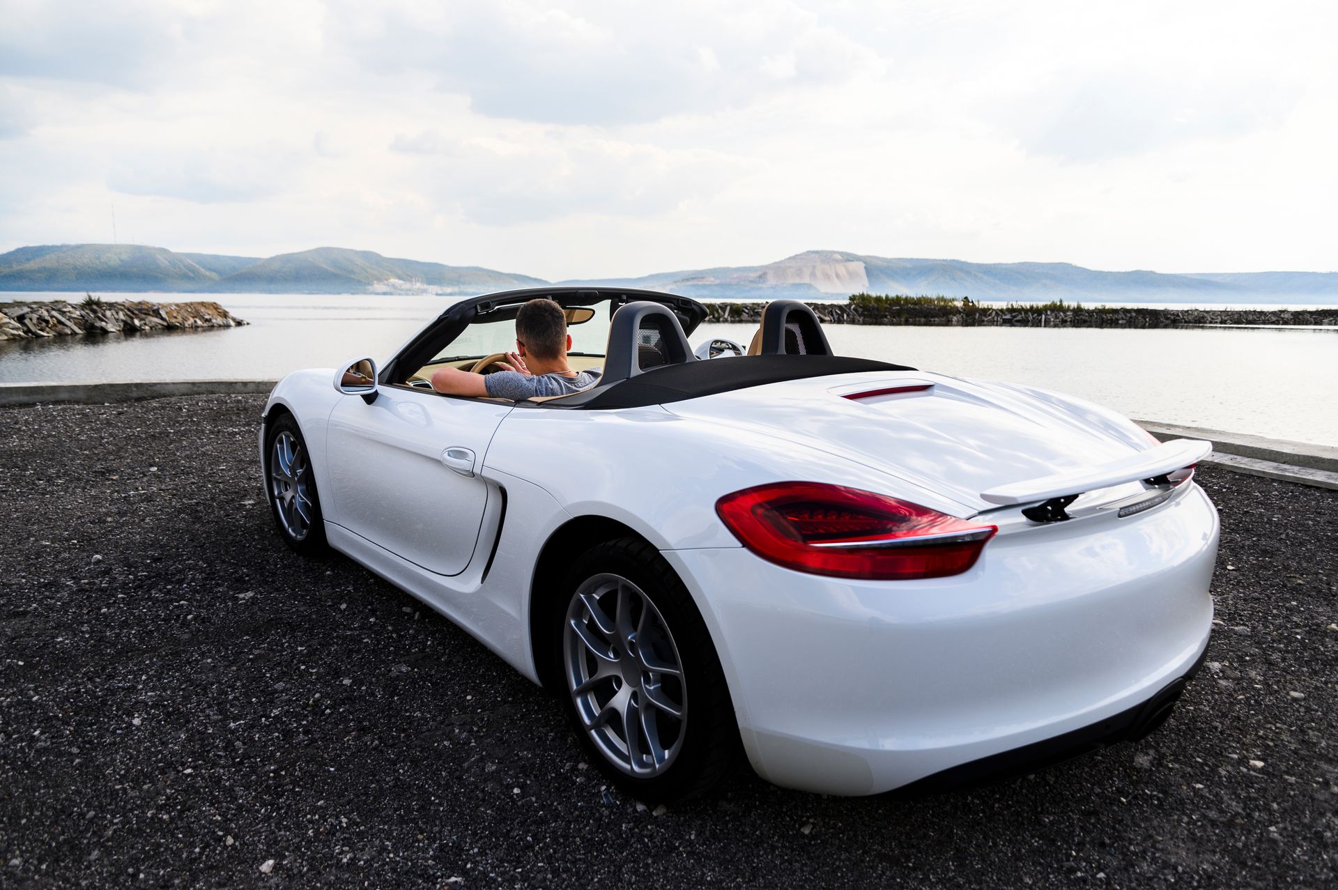 Weißer Porsche Boxter, in der Nähe eines Gewässers geparkt, im Hintergrund Berge.