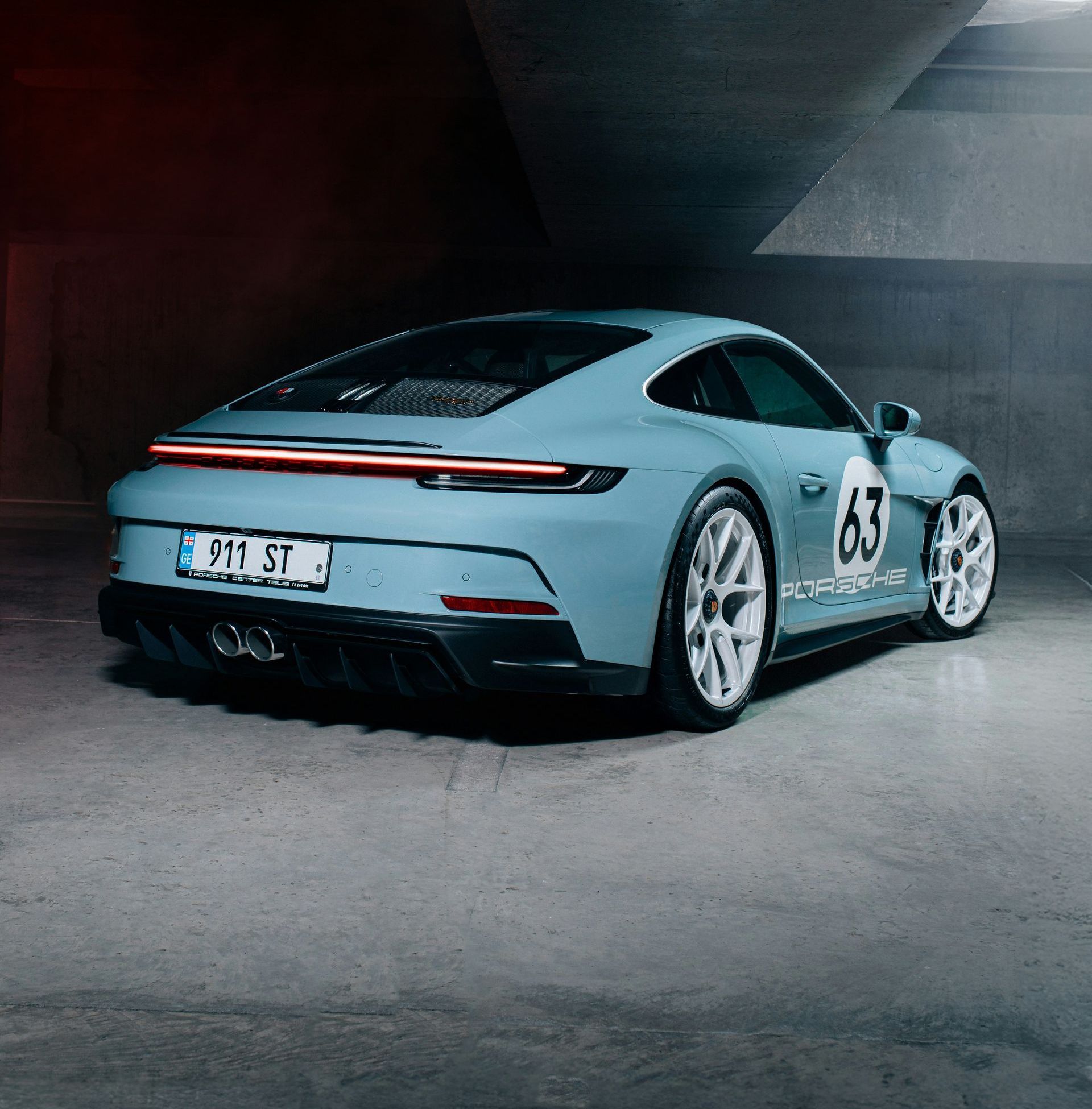 Ein blauer Porsche steht in einer schwarzen Garage mit der Nummer 63 auf der Rückseite.