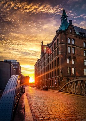 Sonnenuntergang über einer Pflasterstraße mit einem großen, historischen Gebäude und einer brücke in Hamburg, Deutschland.