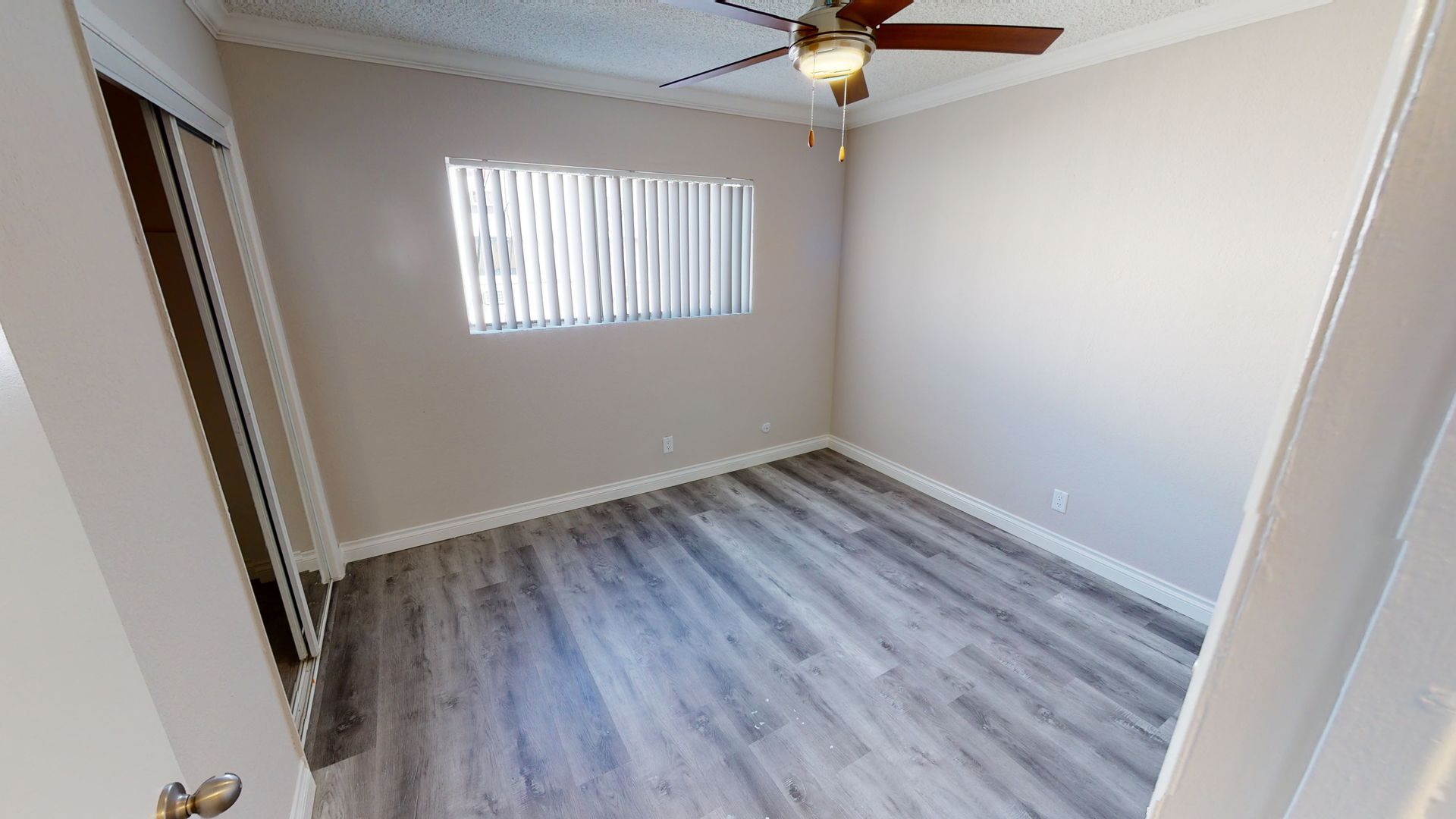 Empty bedroom with gray wood-look floor, window with blinds, and ceiling fan.