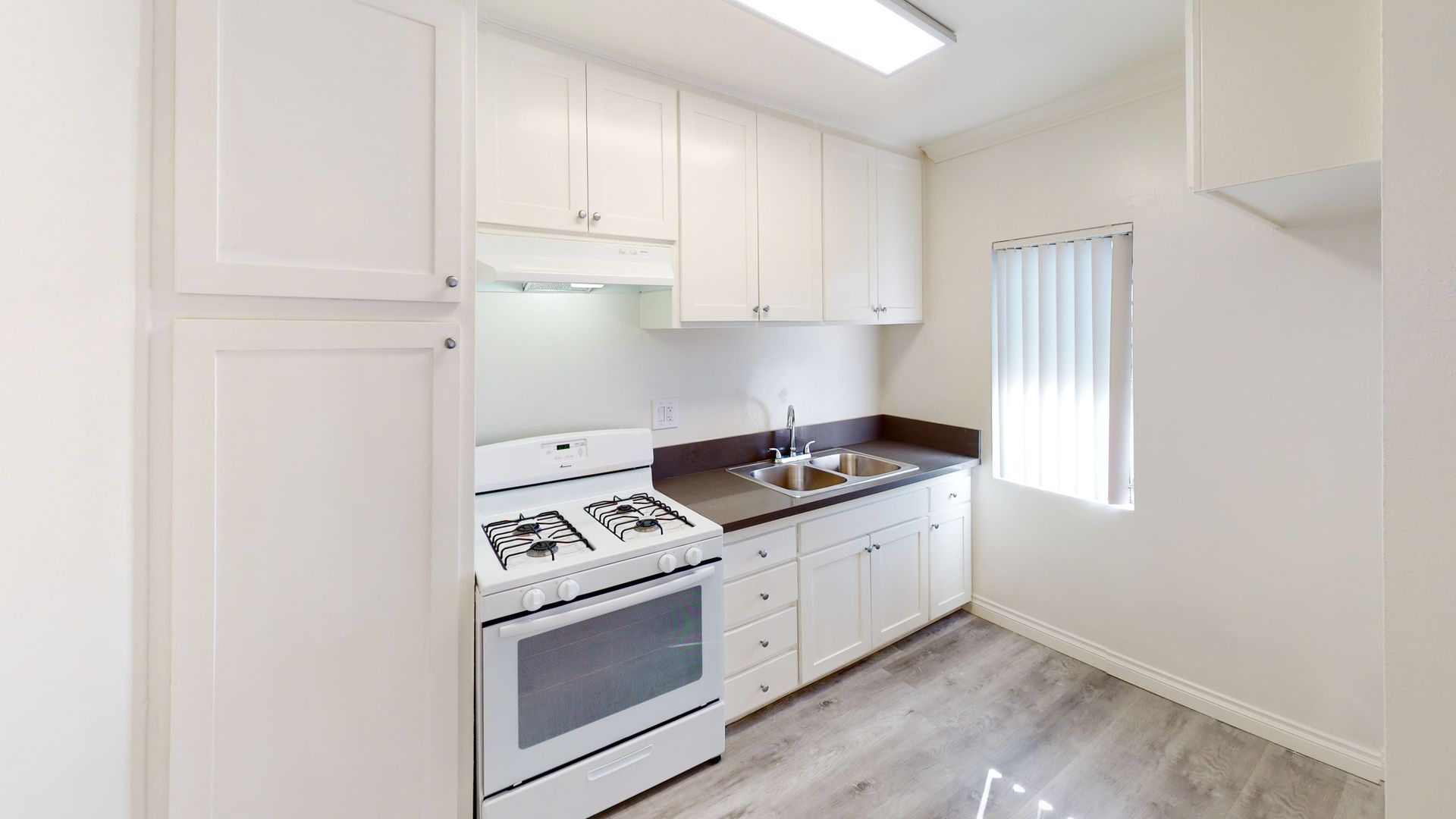 White kitchen with stove, cabinets, sink, and window.
