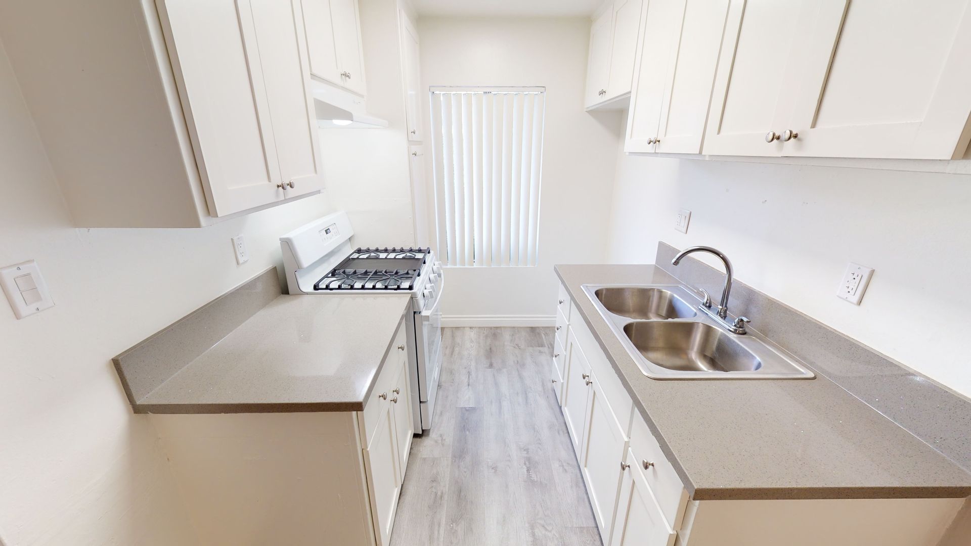 White kitchen with cabinets, stove, sink, and window.