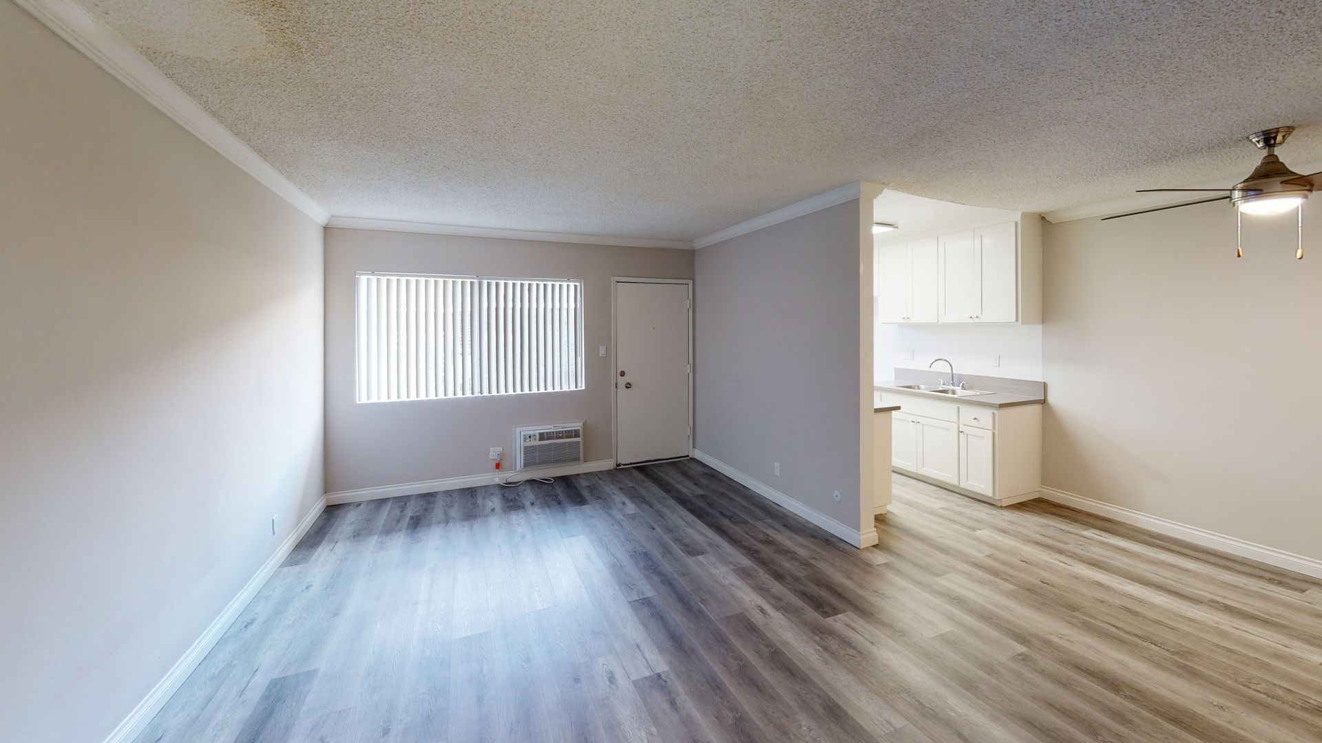 Empty apartment interior with gray walls, wood-look floor, and kitchen in the back.