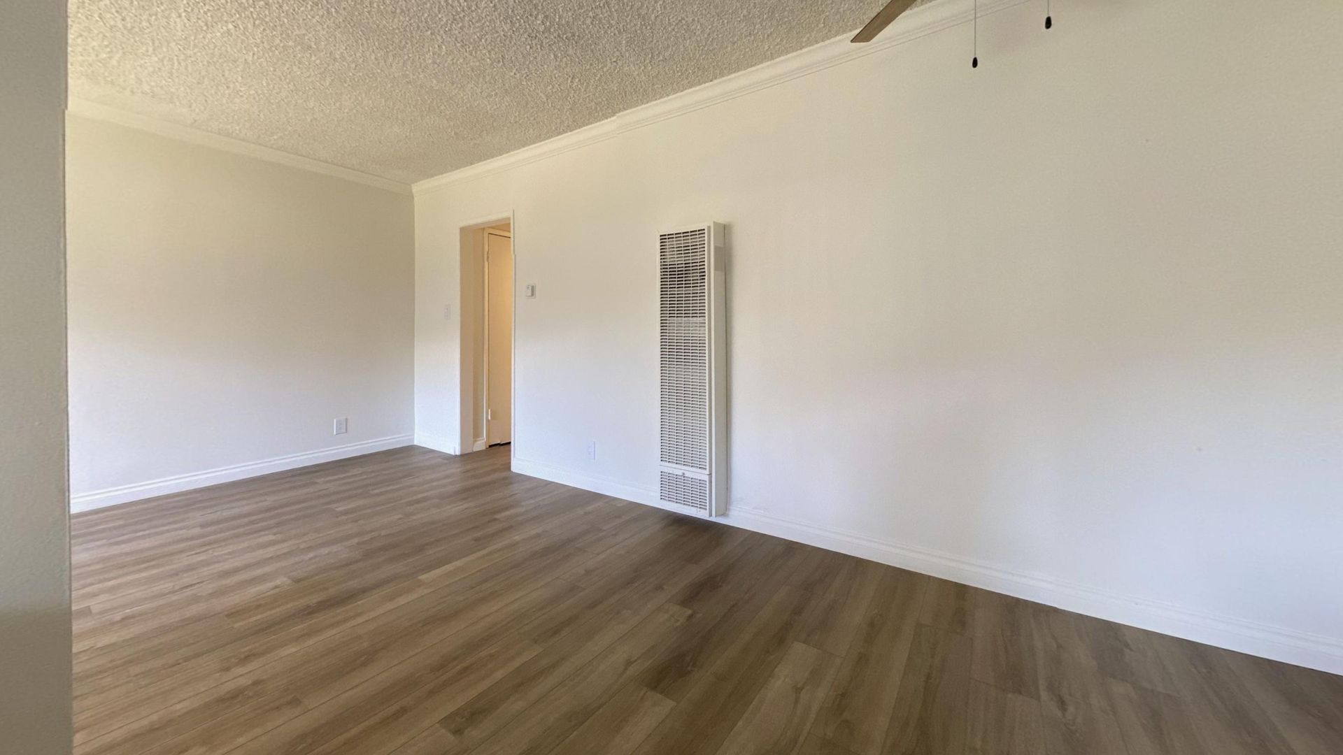 Empty living room with light wood floors, white walls, and a door.