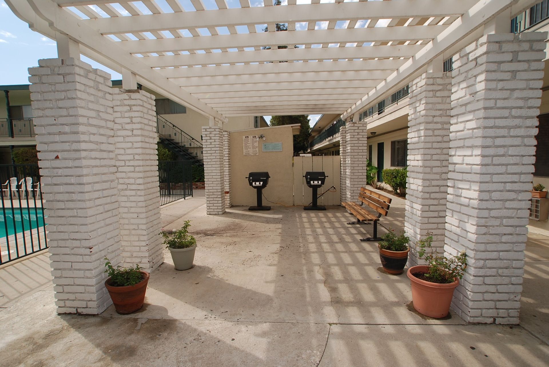 Pergola with white brick pillars, leading to a seating area near a pool.