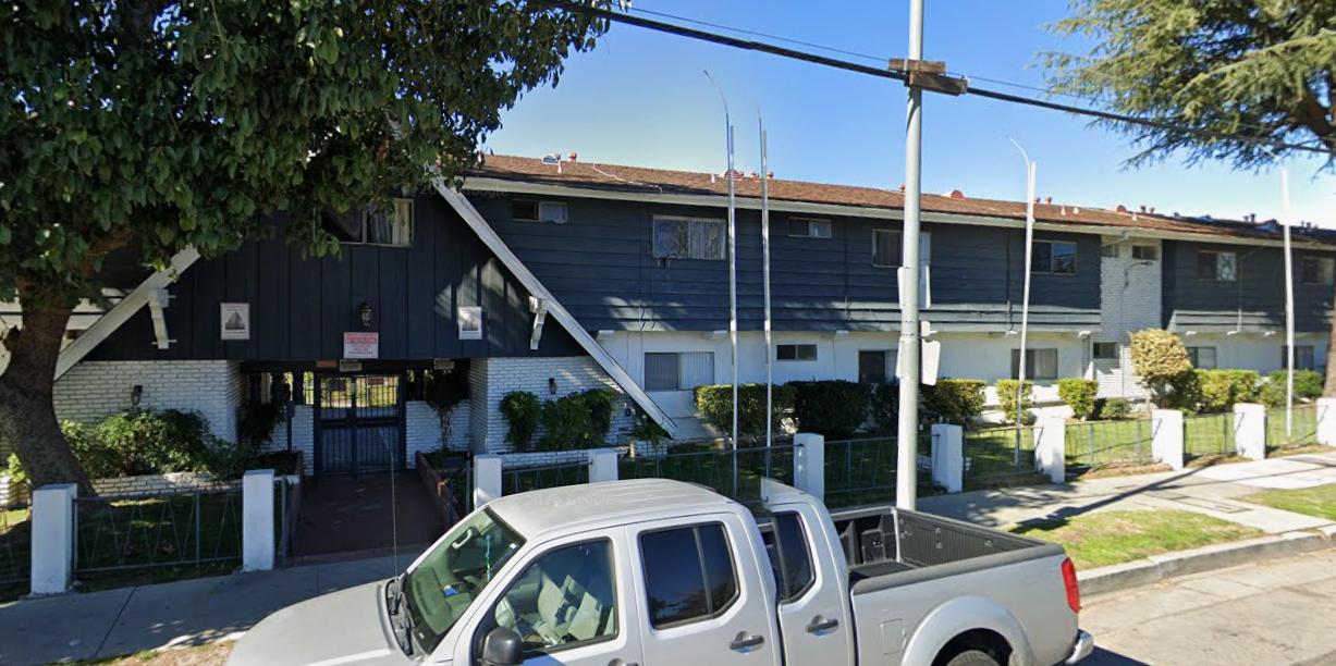 A white pickup truck parked in front of a two-story apartment building with dark trim and white accents.