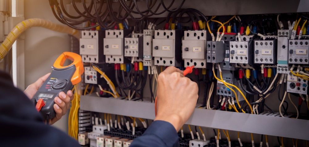 An electrician is working on an electrical panel with a clamp meter.