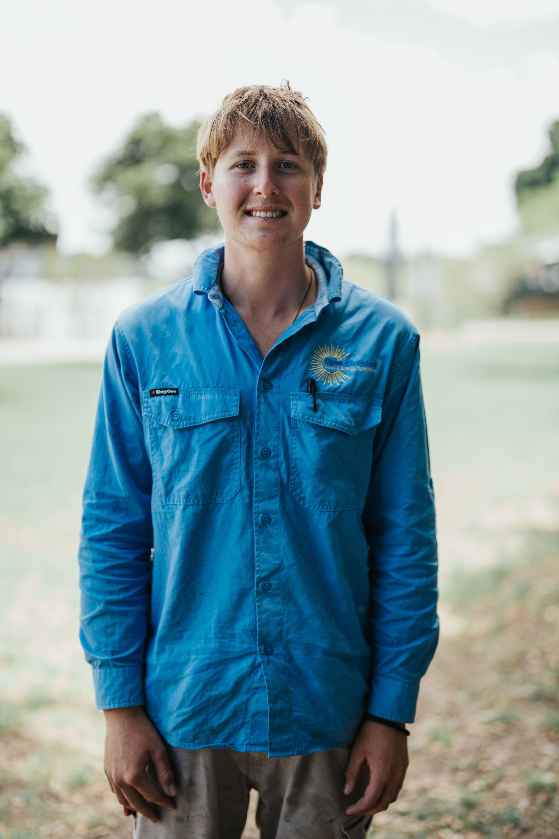 Person in blue work shirt smiles outdoors, soft background.