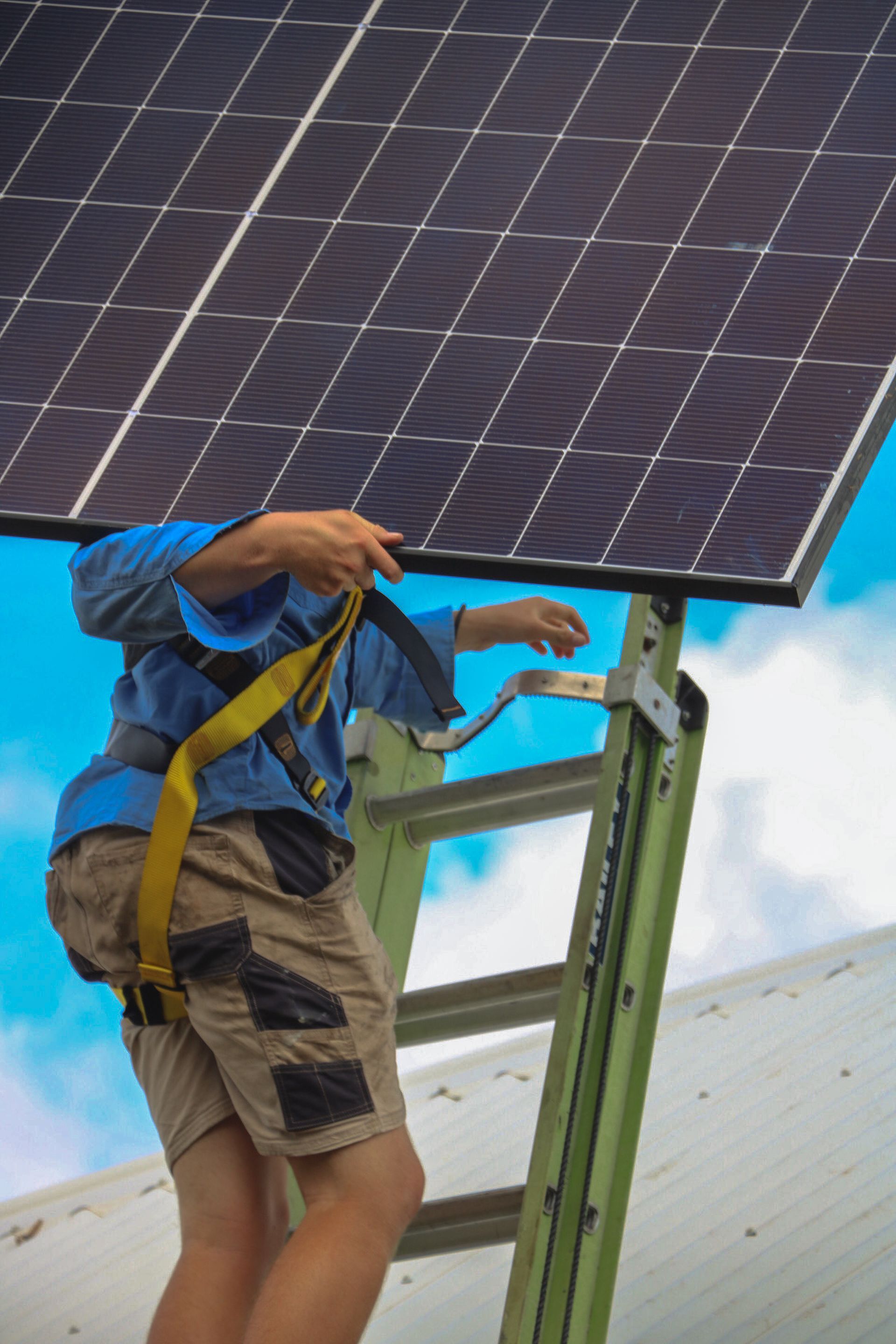 Worker securing rooftop solar panels on a metal frame under a bright blue sky