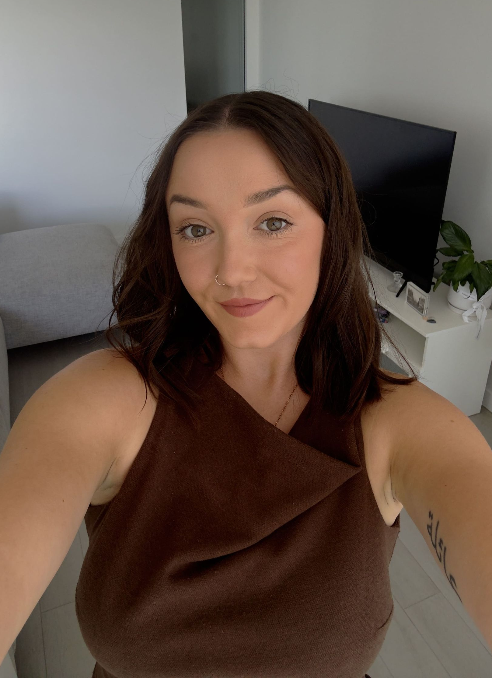 Woman with brown hair and a brown top, smiling at the camera.