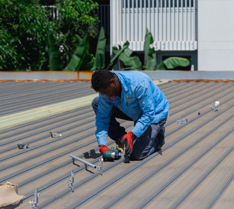 Person in blue shirt on a rooftop installing equipment with a tool.