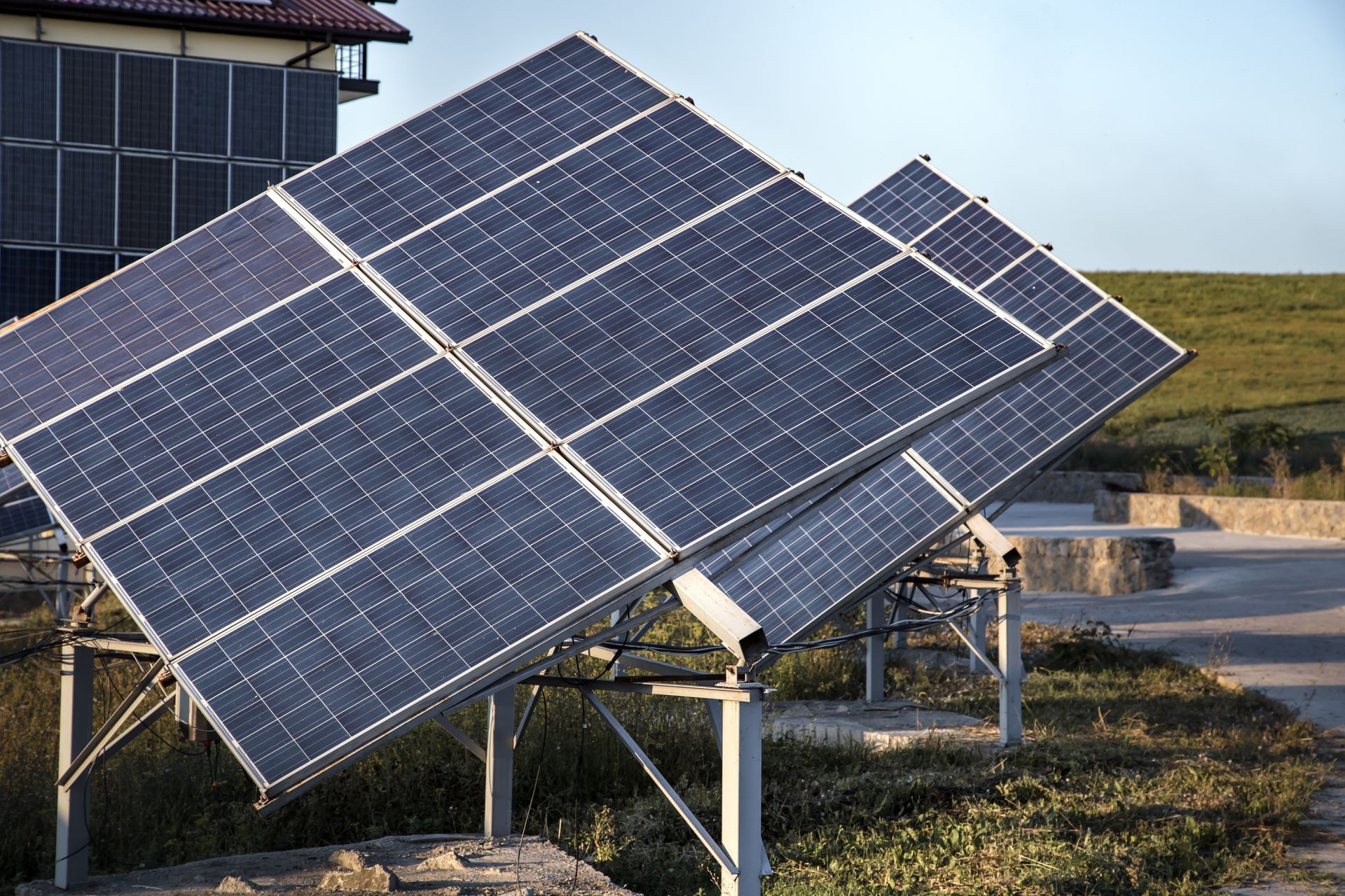 Solar panels tilted toward the sky. Outdoor setting, blue panels, metal frame, building in the background.