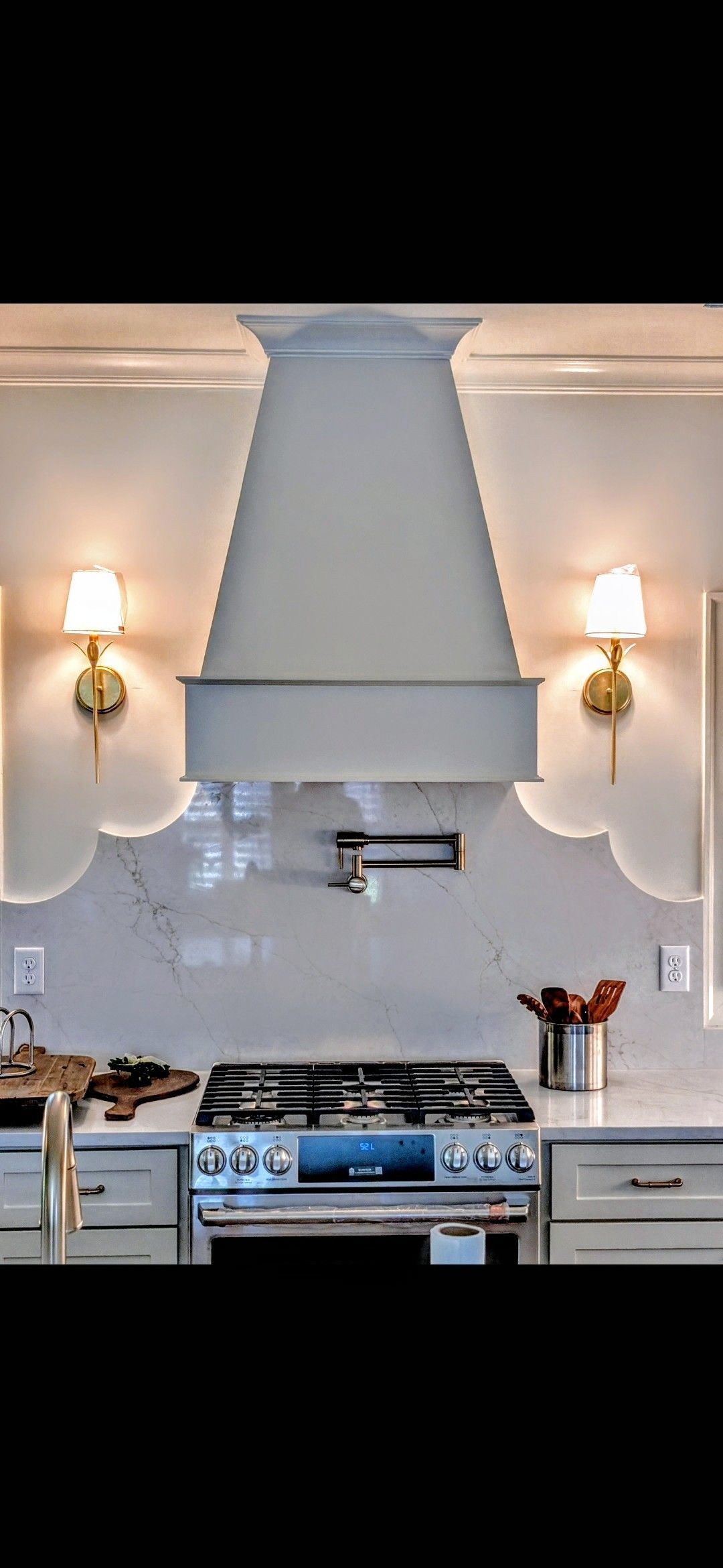 Kitchen with white range hood, stove, and backsplash, flanked by sconce lights.