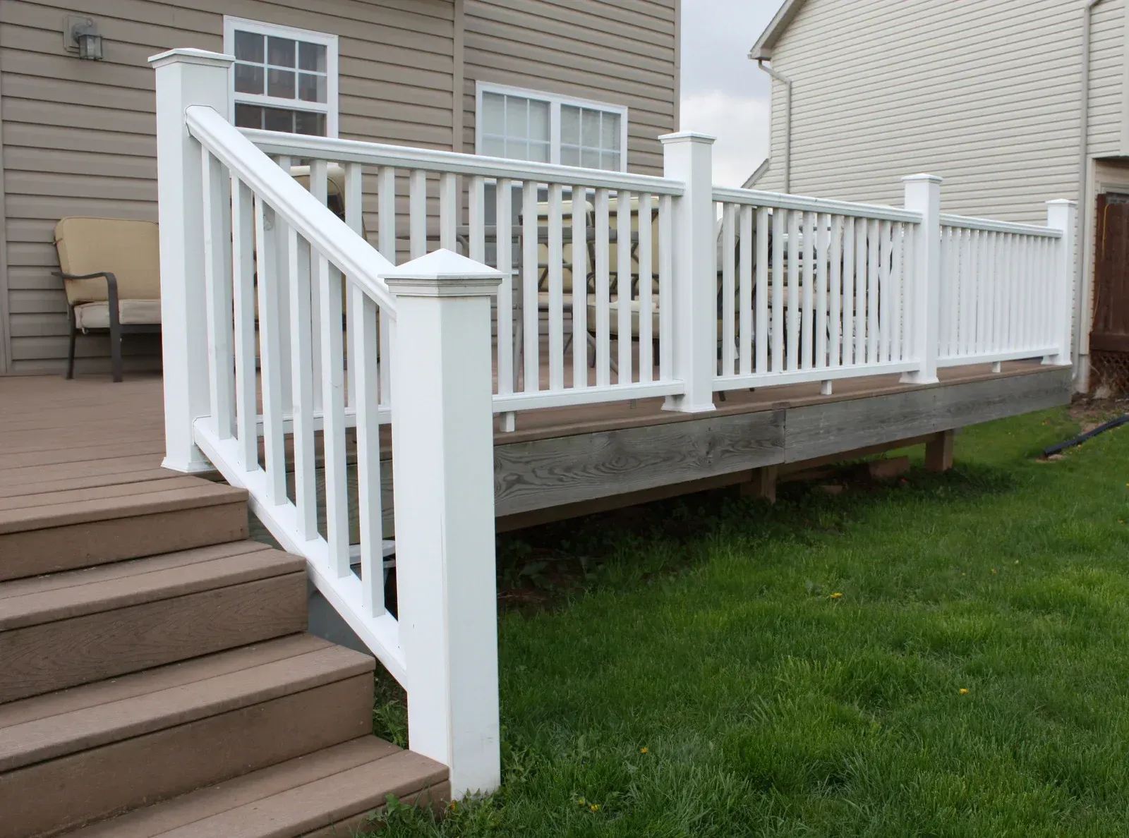 White deck railing and stairs on a raised wooden deck, overlooking a grassy yard.