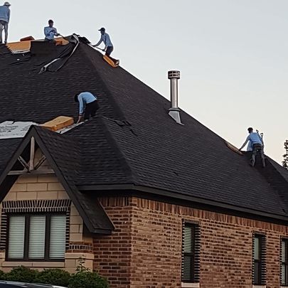 A group of men are working on the roof of a brick house.