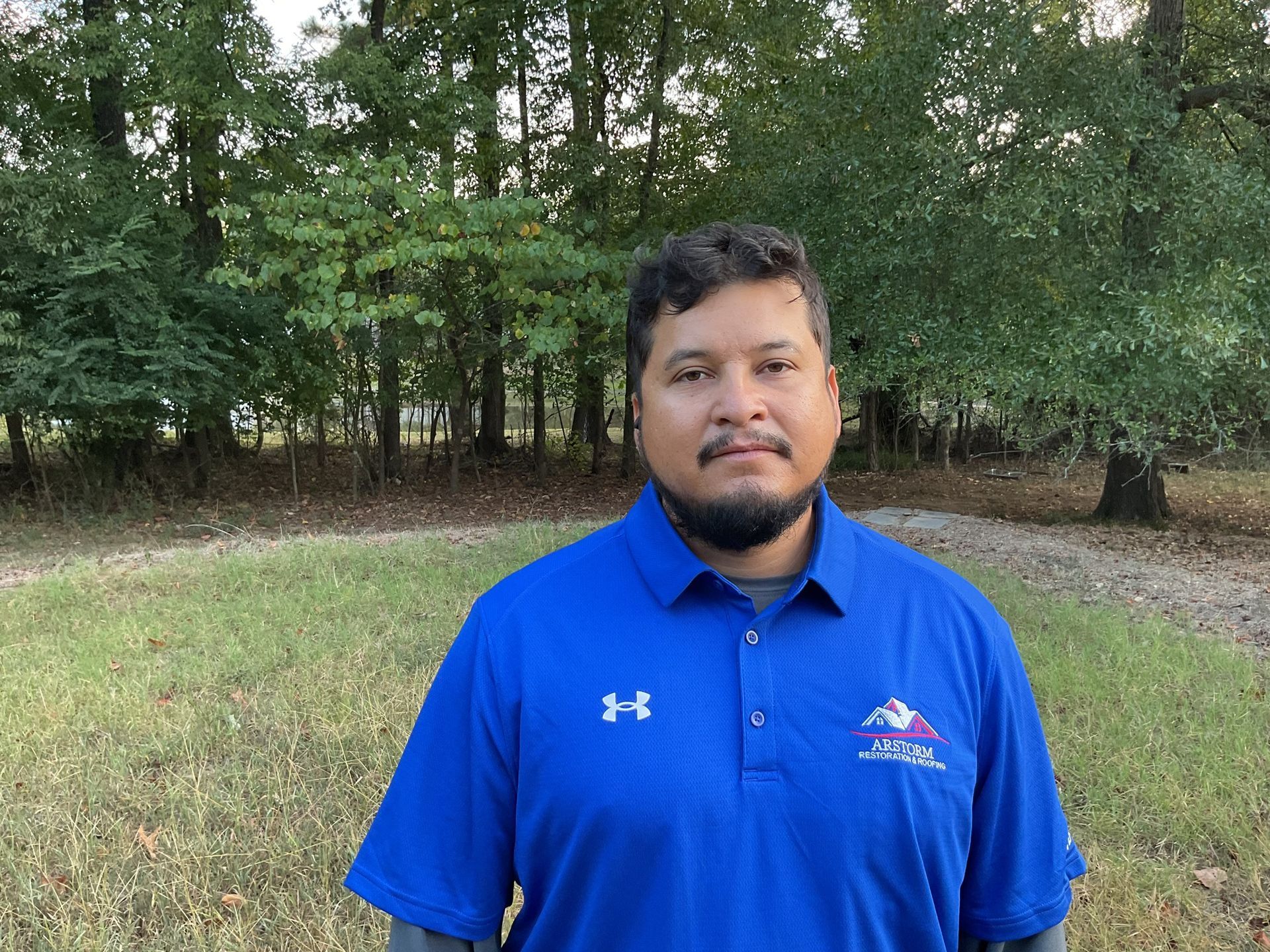 A man in a blue shirt is standing in a field with trees in the background.
