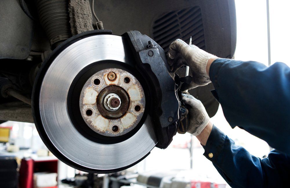 A man is fixing a brake disc on a car in a garage.