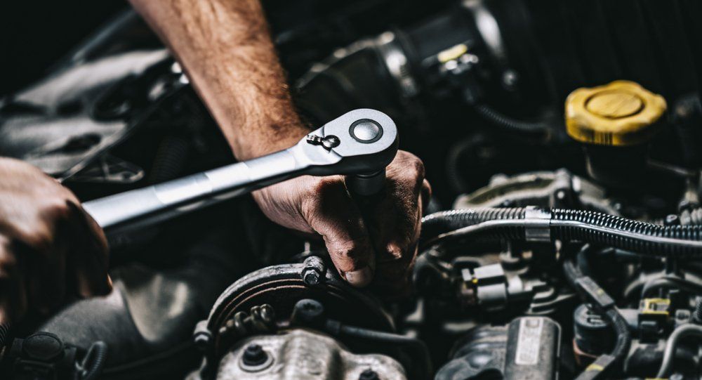 A man is working on a car engine with a wrench.