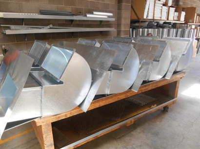 Rows of shiny metal ductwork on a wooden pallet in an industrial workshop