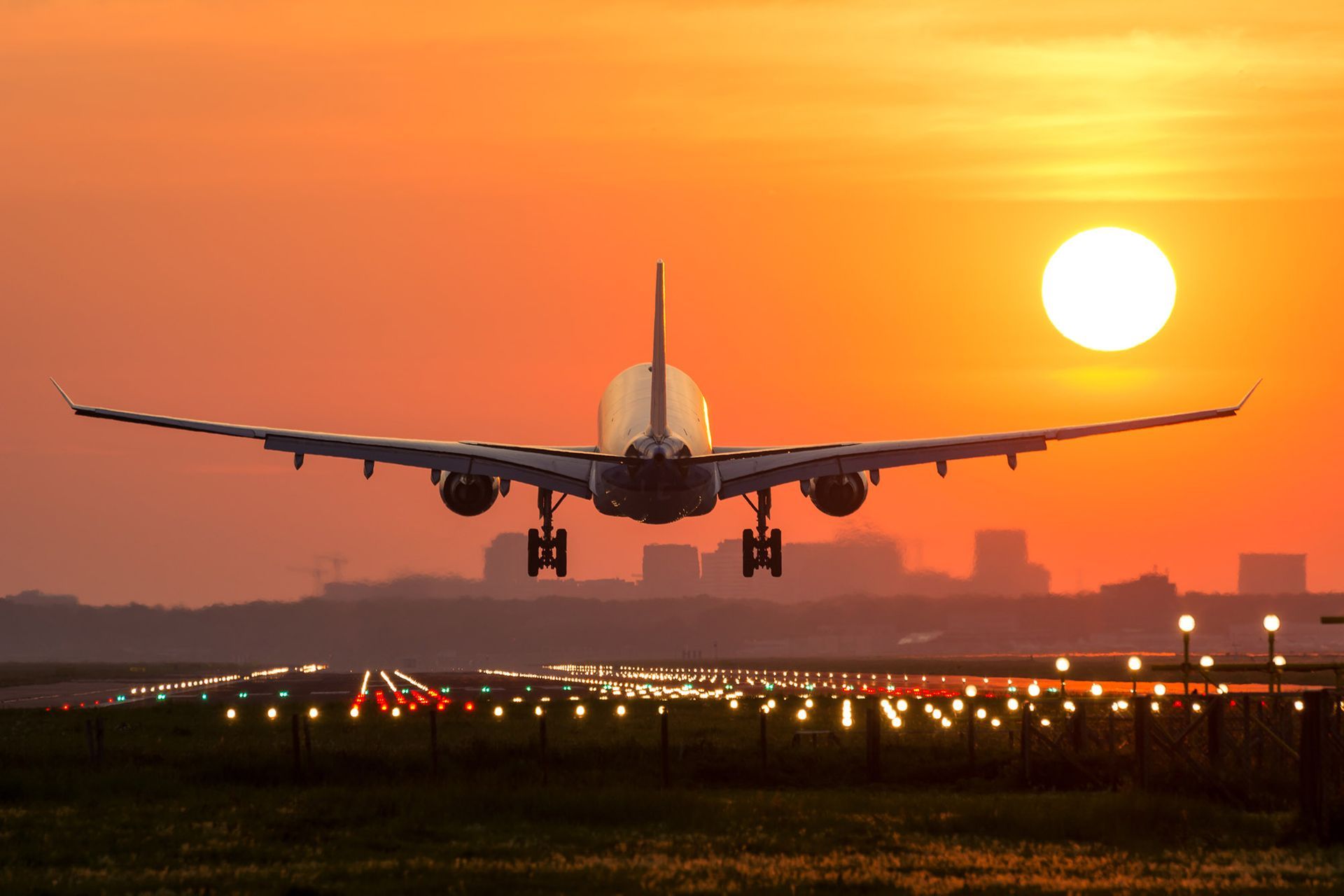 Airplane landing on a runway at sunset; orange sky, bright sun.