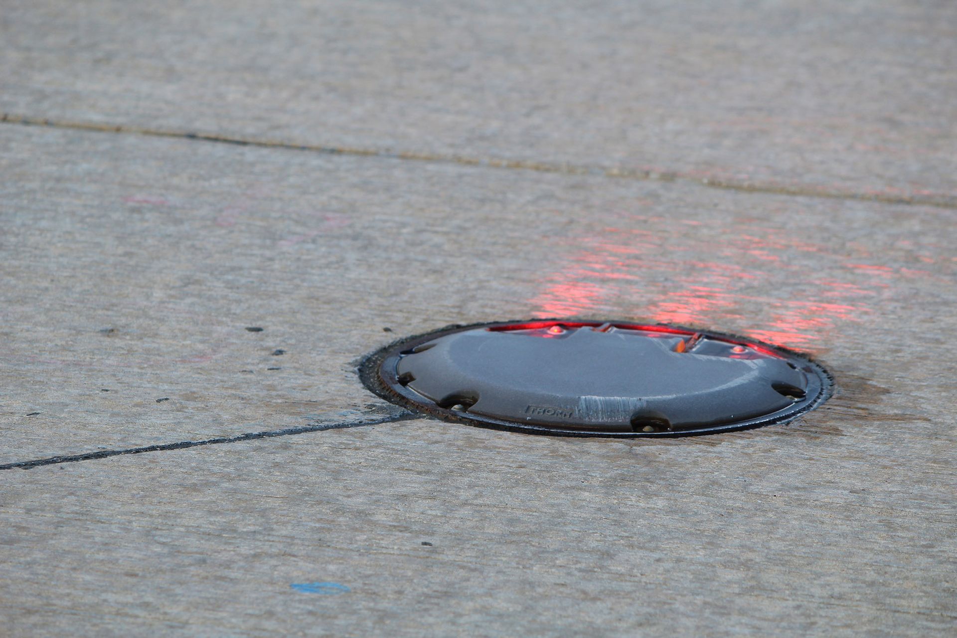 Flush-mounted light fixture in concrete ground emitting orange light.