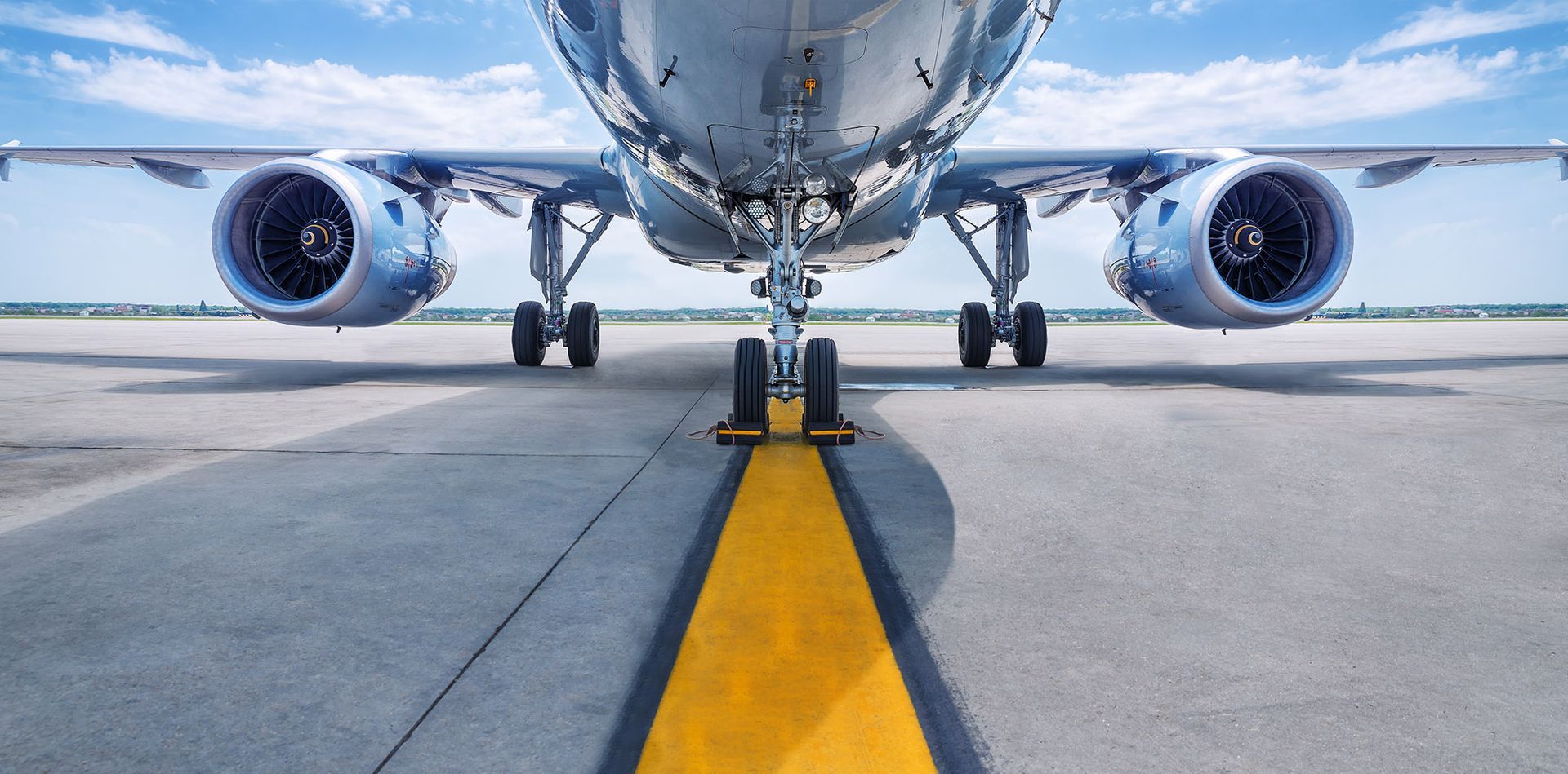 Airplane on a runway, viewed from ground level. Centered on the yellow stripe, engines and landing gear visible.